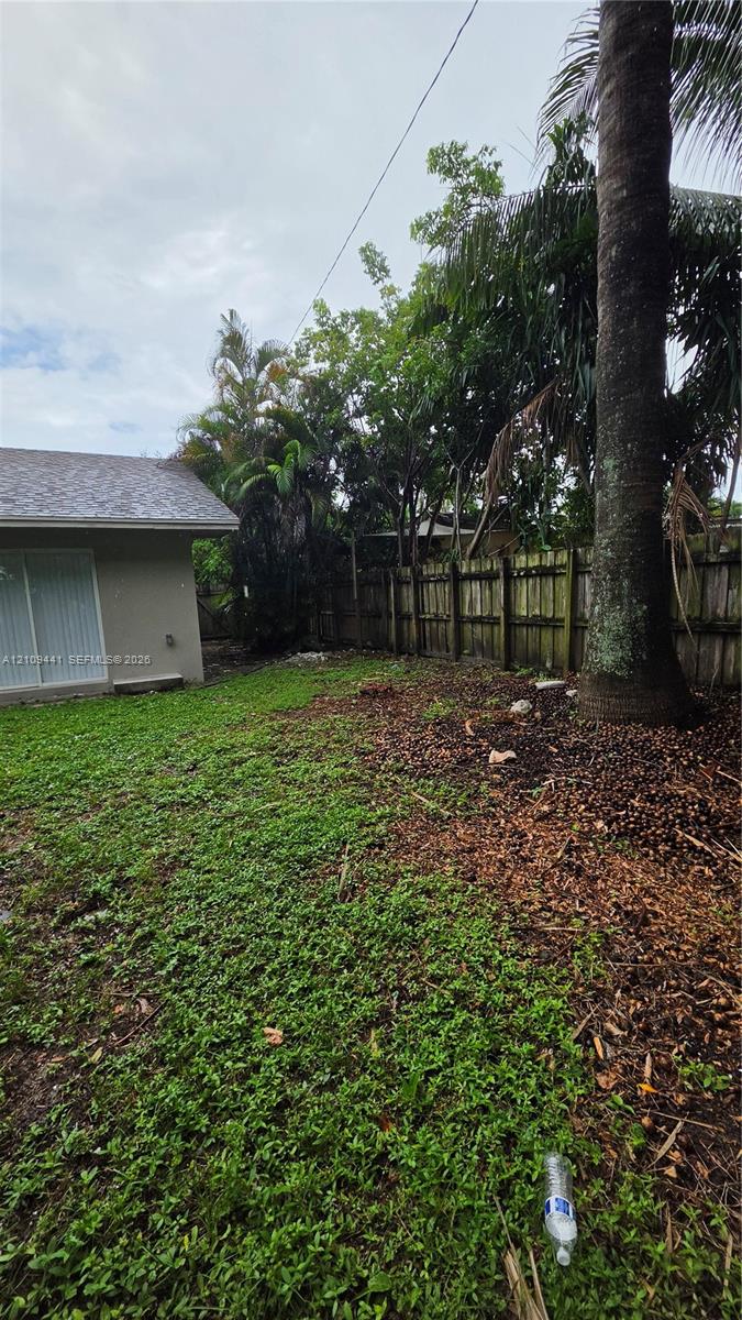 Backyard featuring a wood privacy fence, mature palm trees, and sliding glass door access