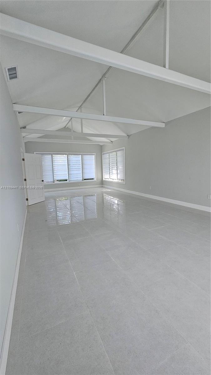 Vaulted ceiling with exposed structural beams, large format light-toned tile flooring, and multiple windows with white horizontal blinds