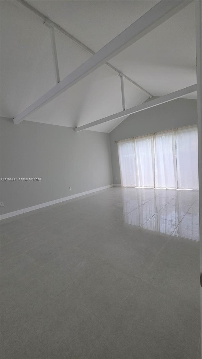 Vaulted ceiling featuring exposed structural beams, high-gloss tile flooring, and floor-to-ceiling windows