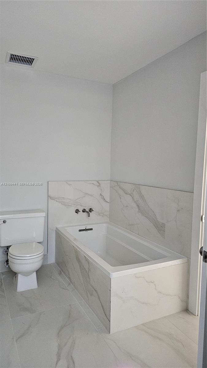 Bathroom featuring a deep soaking tub with a wall-mounted faucet, complemented by large-format tile flooring and matching tile surround