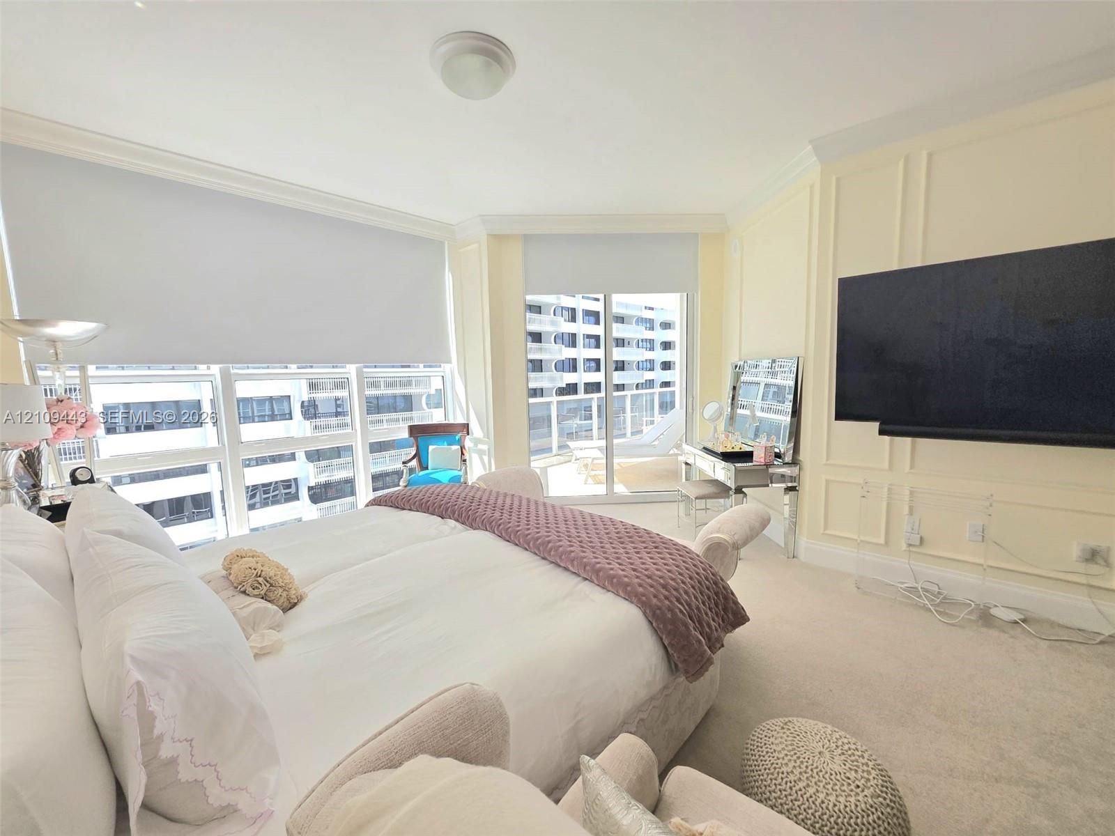 Expansive floor-to-ceiling windows, sliding glass door access to a private balcony, custom wall molding, neutral carpeting, and a ceiling-mounted light fixture