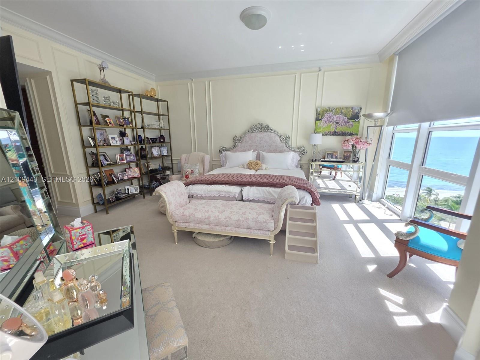 Floor-to-ceiling windows with coastal horizon, walls featuring custom crown molding and picture frame wainscoting, and carpeted flooring