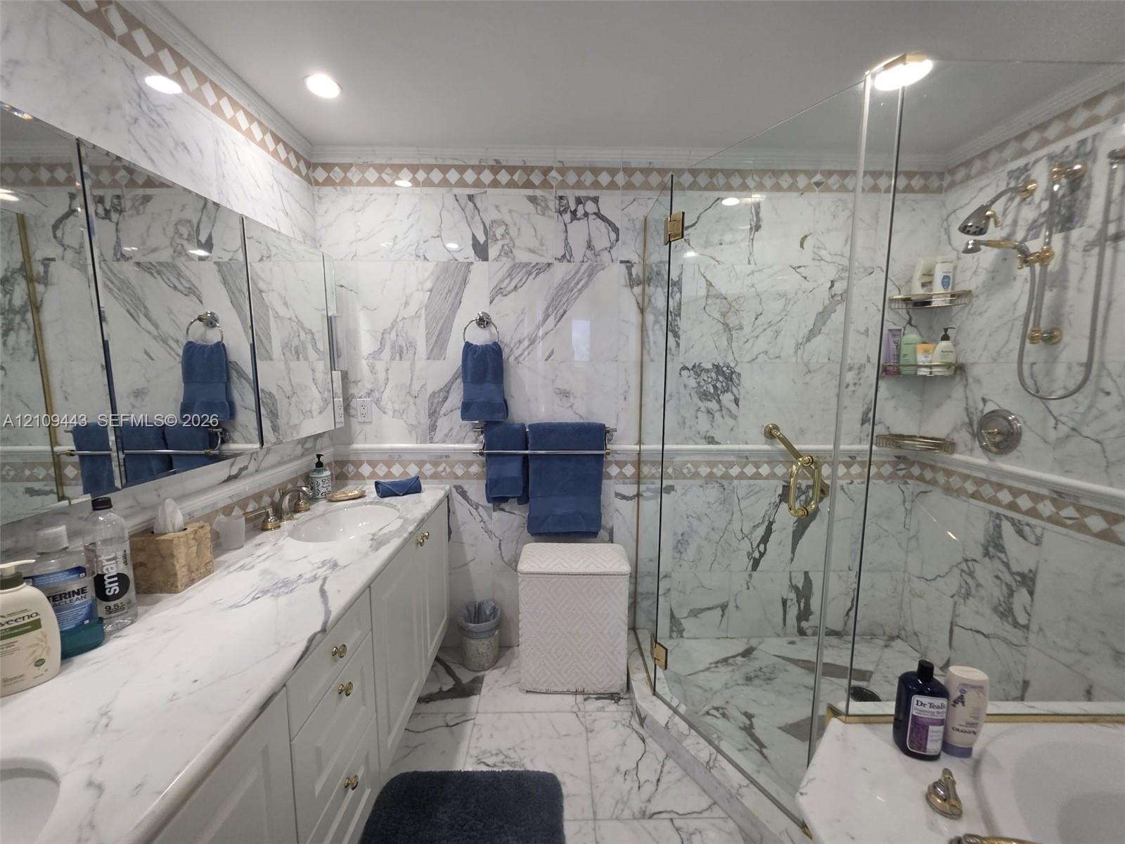 Bathroom featuring full-height stone wall tiling, a double vanity with stone countertop, recessed lighting, and a walk-in glass-enclosed shower with gold-tone hardware