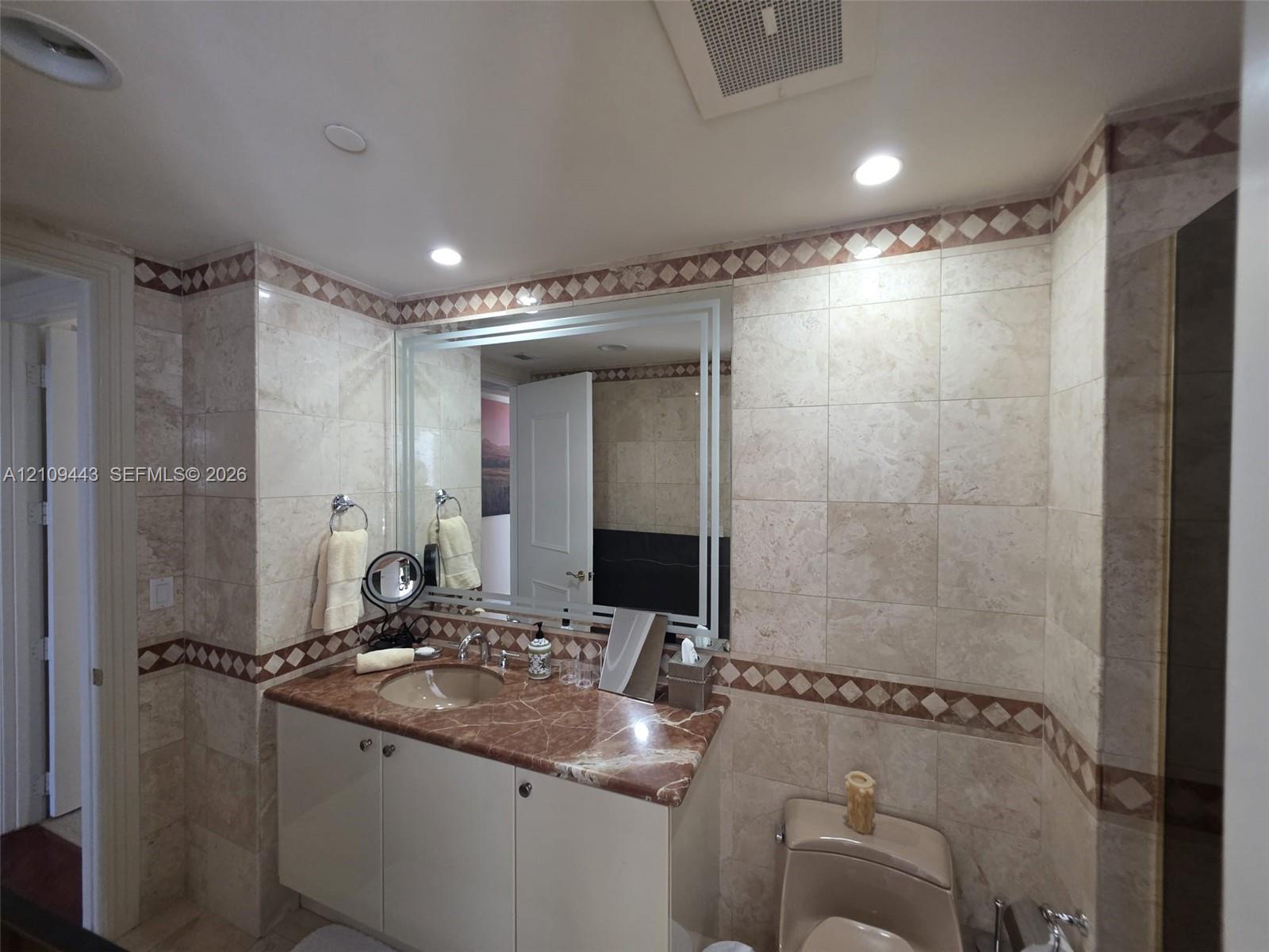 Vanity featuring a stone countertop with an integrated basin, neutral tile wall cladding, and decorative diamond-patterned tile inlay