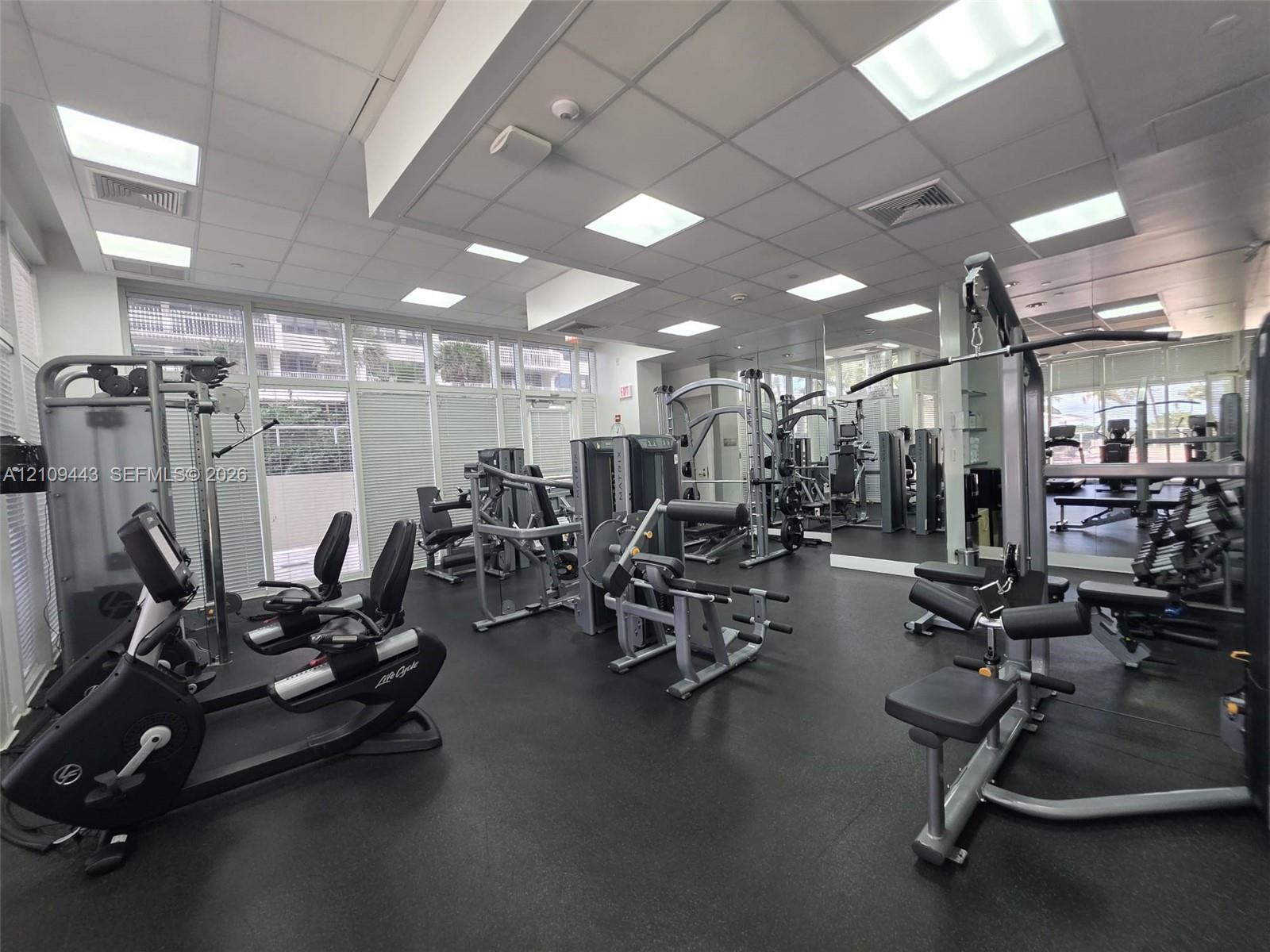Fitness center featuring recessed square lighting, wall-to-wall mirrors, rubberized flooring, and expansive windows