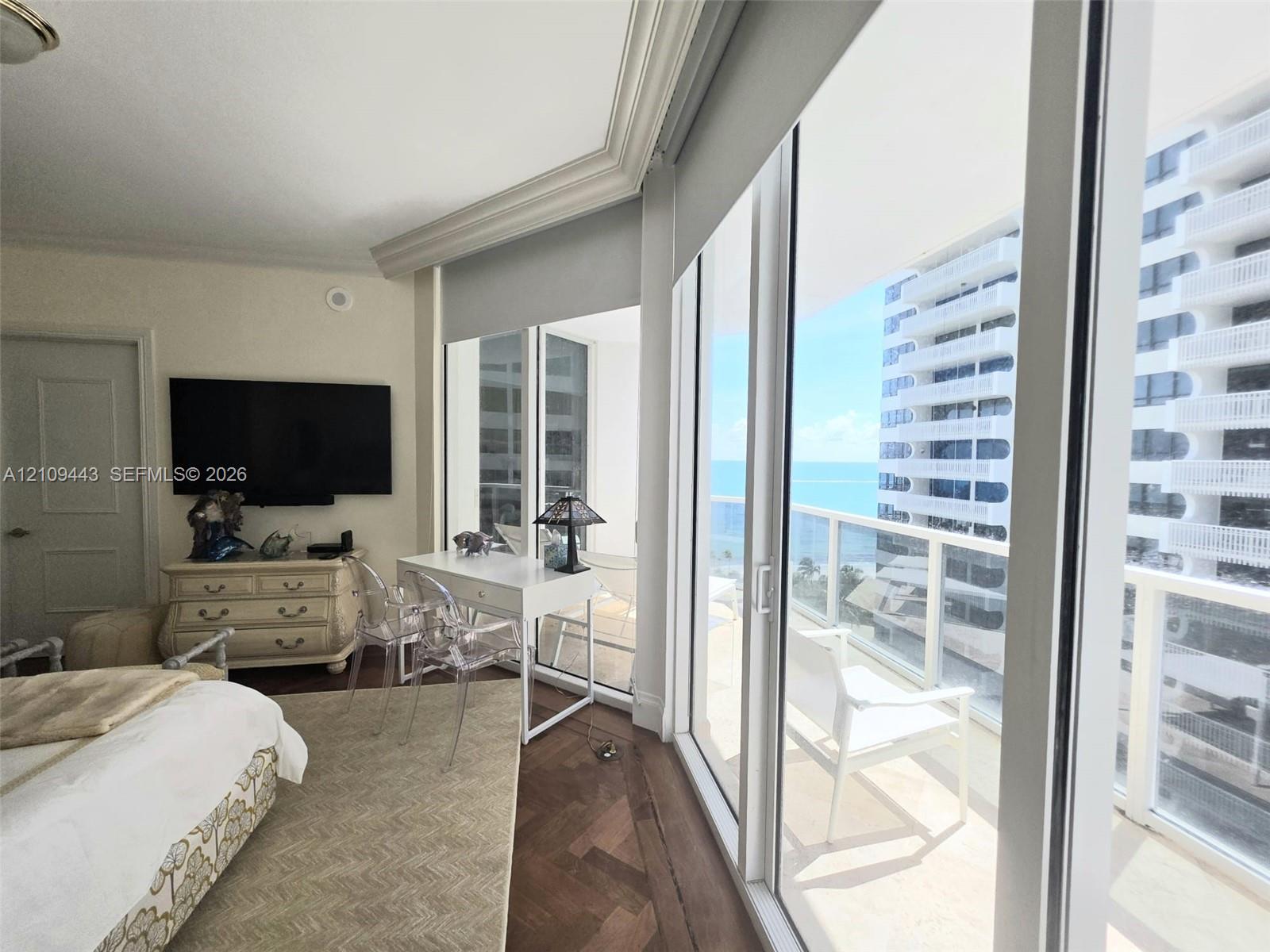 Floor-to-ceiling glass sliding doors, wood-finish flooring in a herringbone pattern, crown molding, and a private balcony featuring a glass panel railing