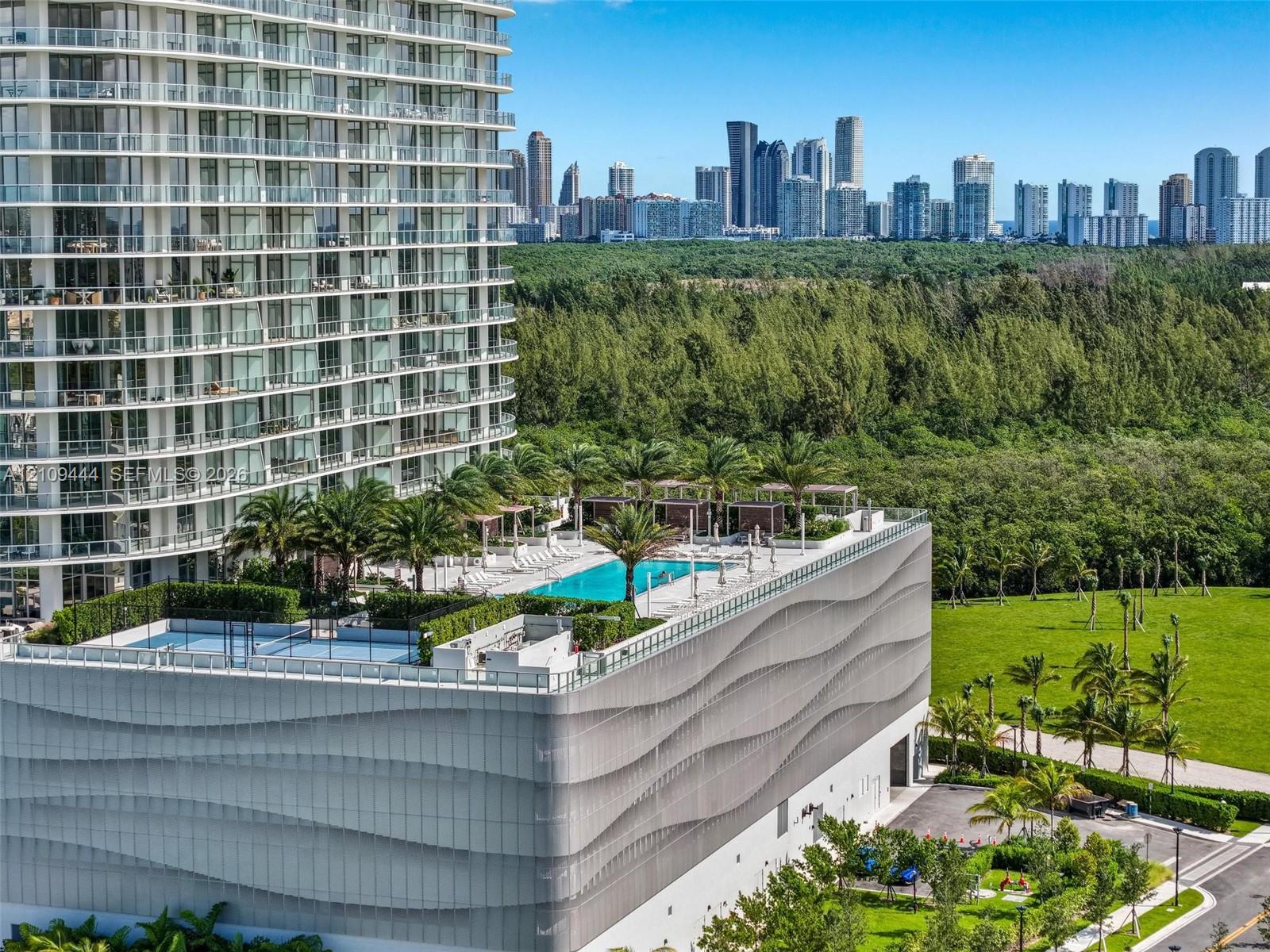 High-rise residential complex featuring an elevated pool deck, a recreational court, landscaped green space, and a decorative undulating facade