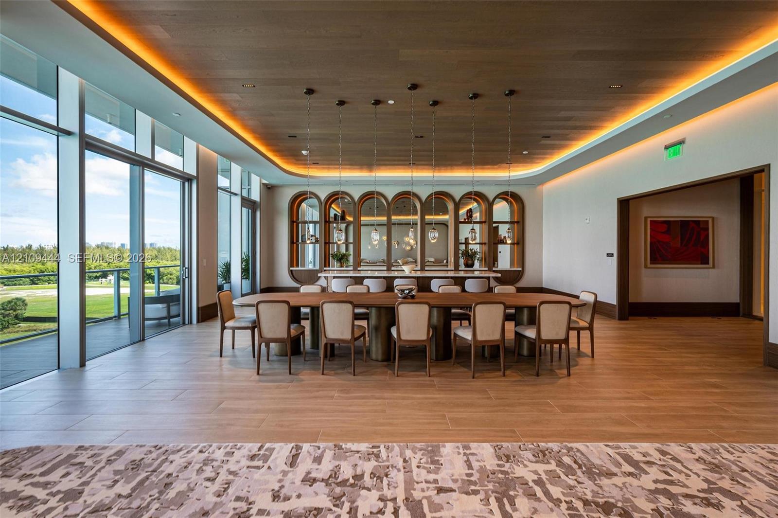 Floor-to-ceiling glass windows, wood-finish ceiling with cove lighting, custom arched built-in shelving, stone-topped bar, and large-format tile flooring