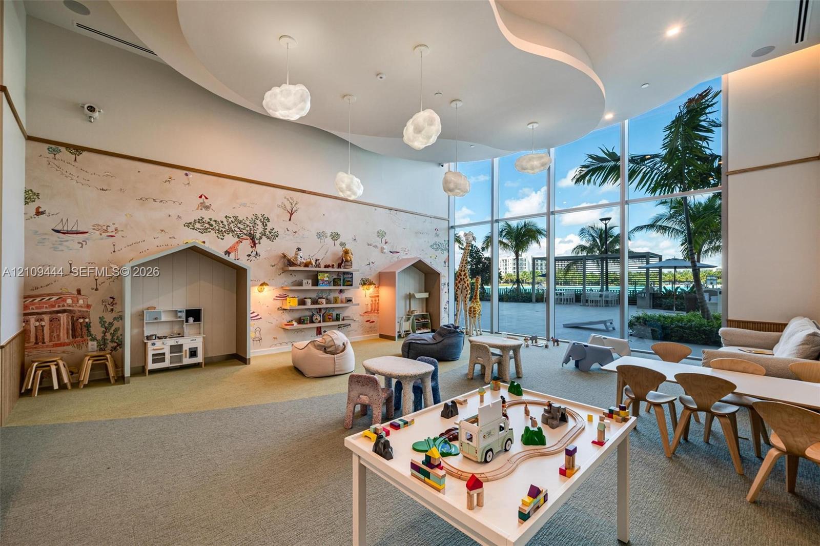 Floor-to-ceiling windows, custom built-in wall alcoves, decorative wall mural, sculpted tray ceiling with recessed lighting, and suspended cloud-style pendant fixtures