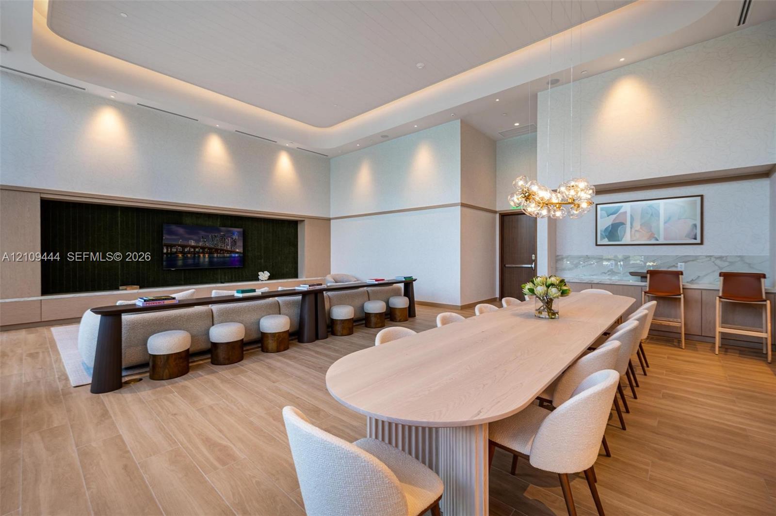 High-ceiling interior featuring recessed tray lighting, wood-finish flooring, a built-in entertainment niche, and a custom bar area with stone-finish surfacing and integrated lighting