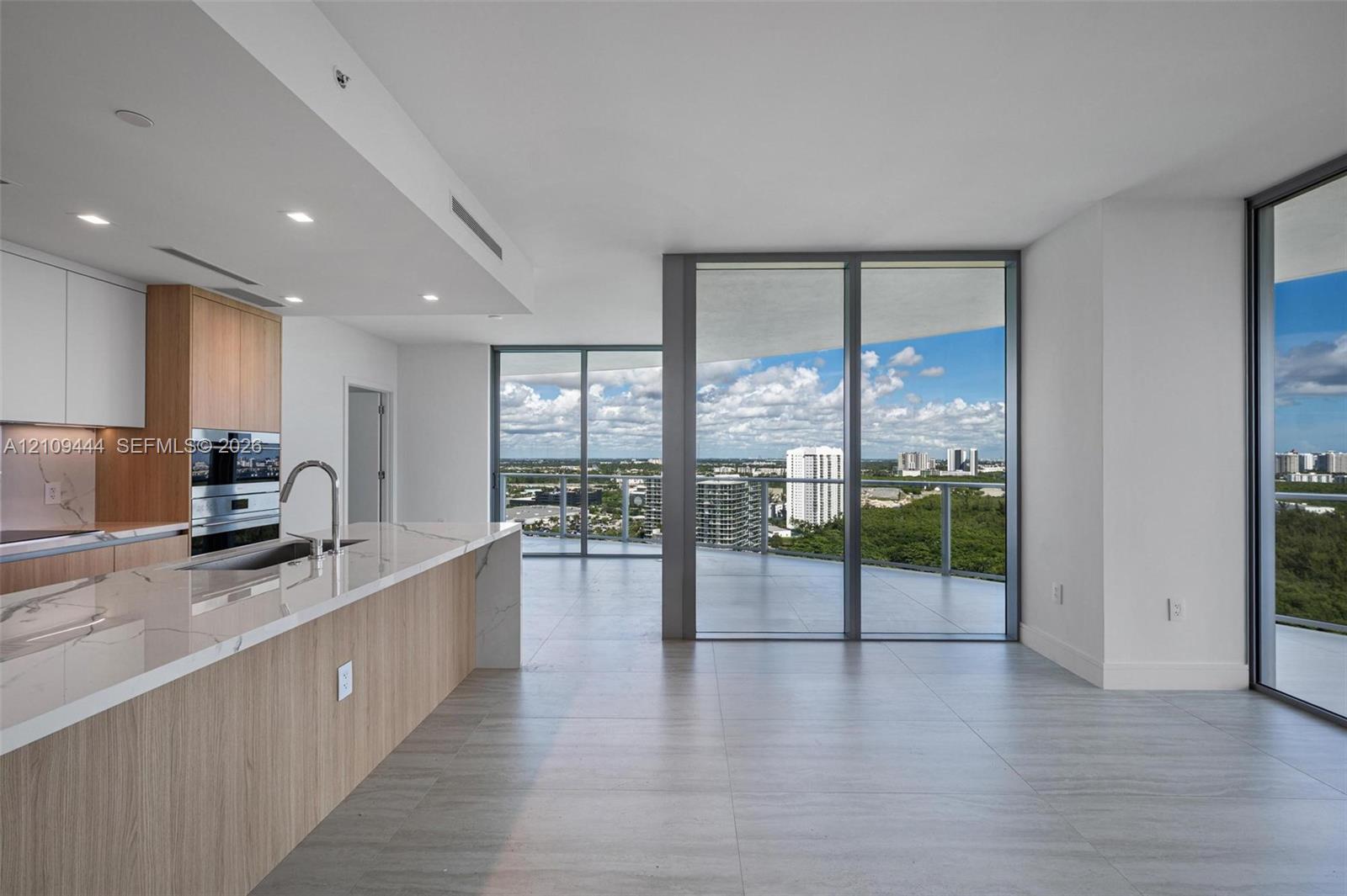 Kitchen featuring wood-finish cabinetry, stone countertops, built-in double ovens, and expansive floor-to-ceiling glass panel doors opening to a wrap-around balcony with exterior horizon scenery