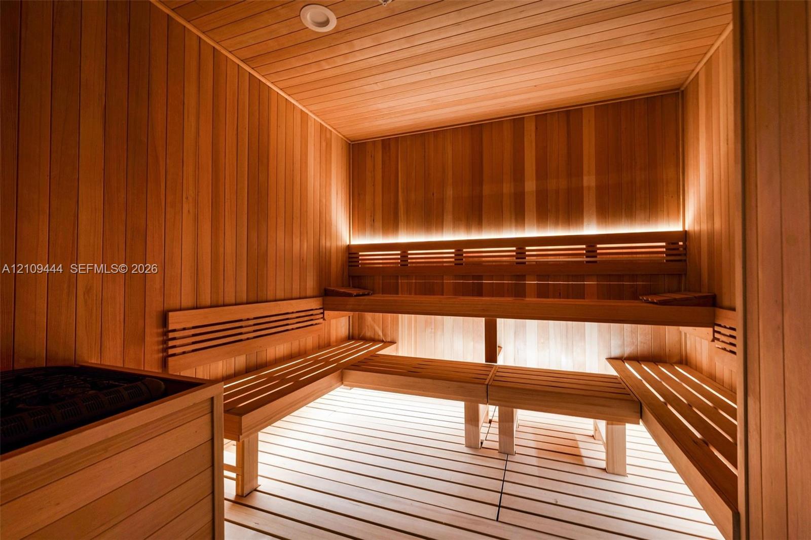 Sauna featuring wood-plank wall paneling, multi-level slatted wood benches, hidden LED accent lighting, and a built-in heating unit