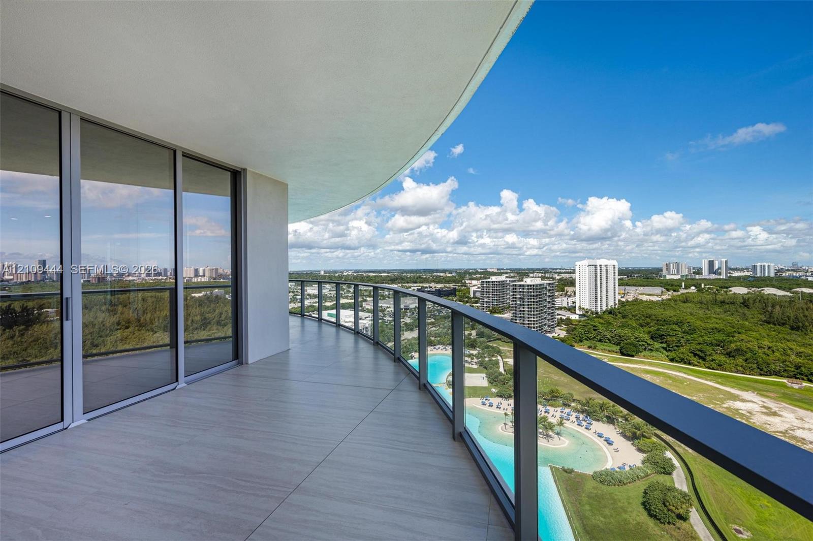Curved balcony featuring large-format tile flooring, metal railings, glass panels, and floor-to-ceiling sliding glass doors