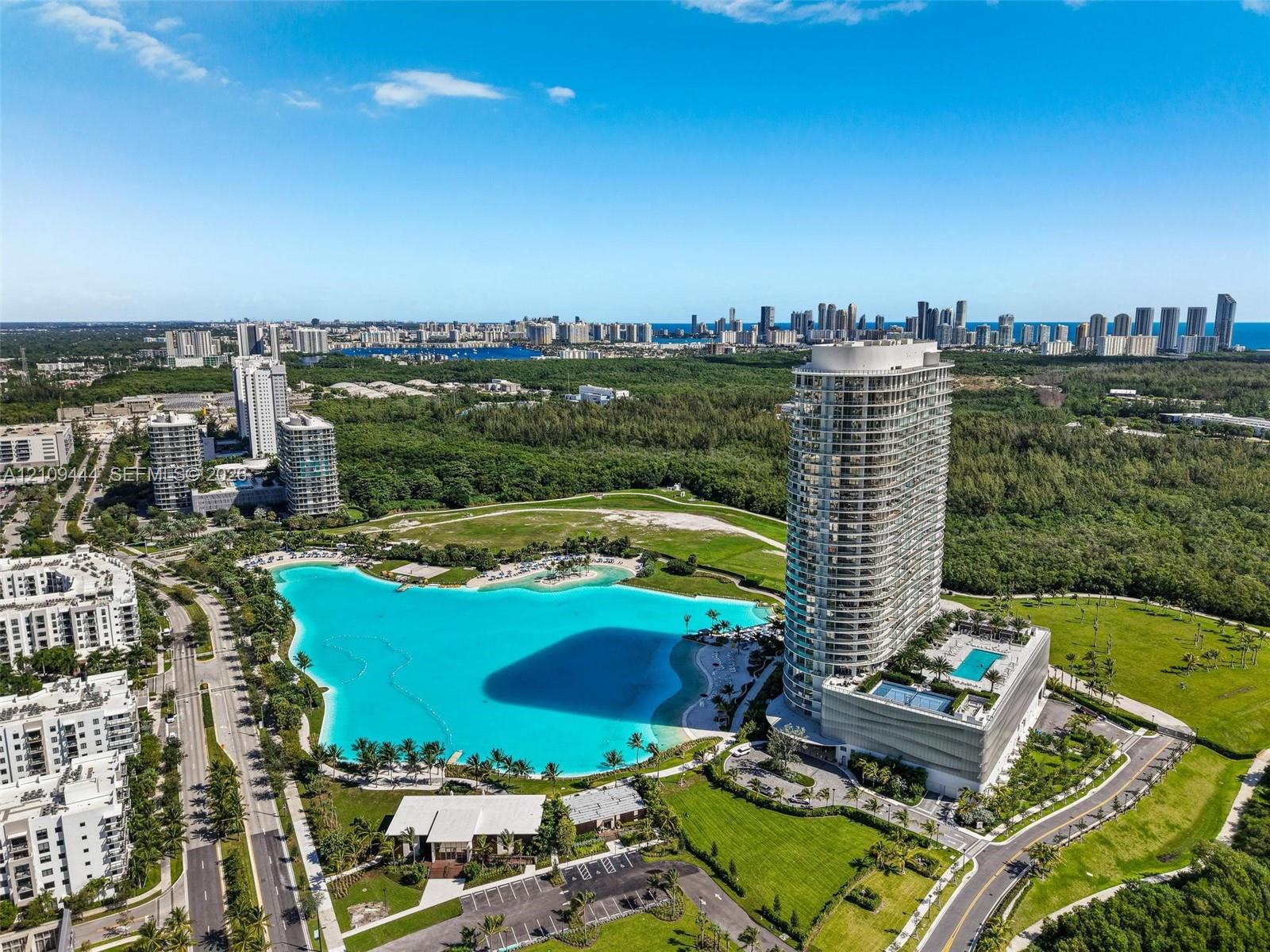 Aerial perspective of a high-rise residential tower featuring a multi-level podium, an attached swimming pool, landscaped grounds, and a central lagoon