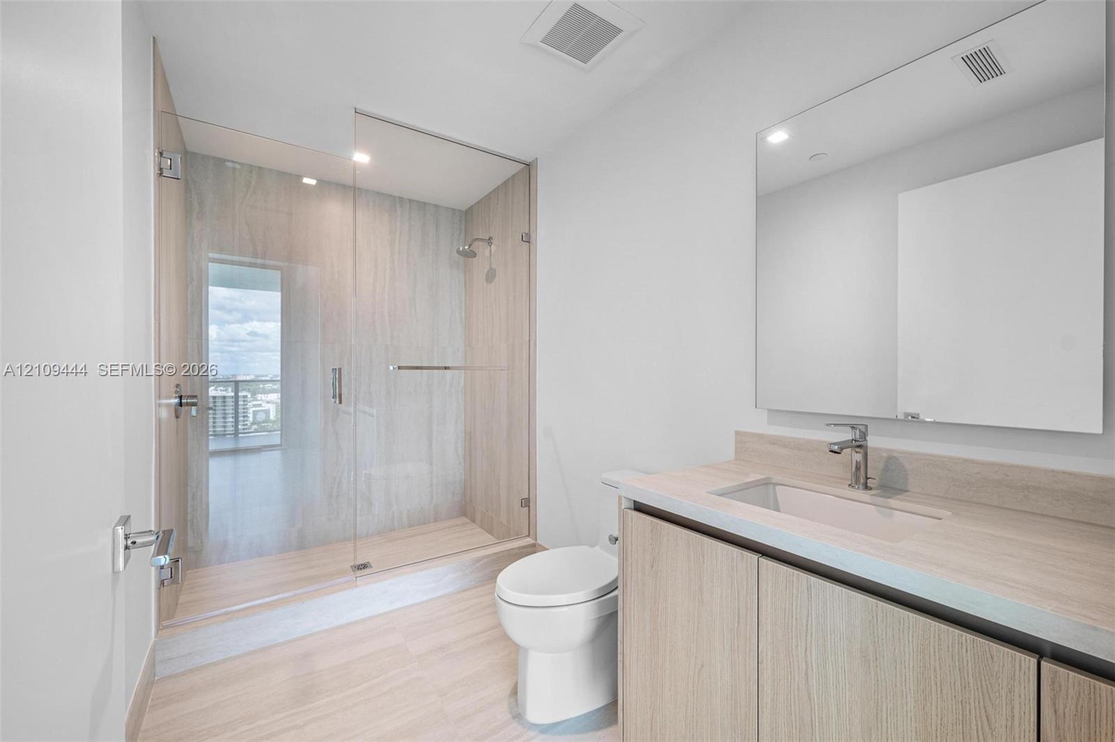 Bathroom featuring wood-finish cabinetry, a large integrated mirror, a walk-in shower with a glass enclosure and floor-to-ceiling wall tile, and light-toned flooring