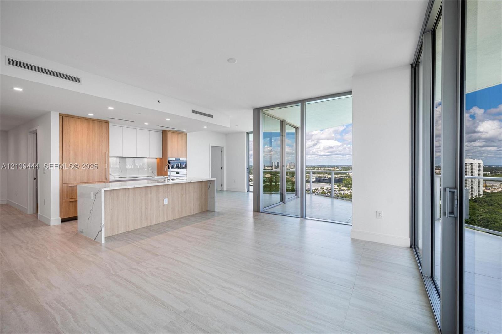 Open-concept kitchen featuring wood-finish cabinetry, a waterfall-edge stone island, built-in stainless steel appliances, wood-finish flooring, and floor-to-ceiling glass doors