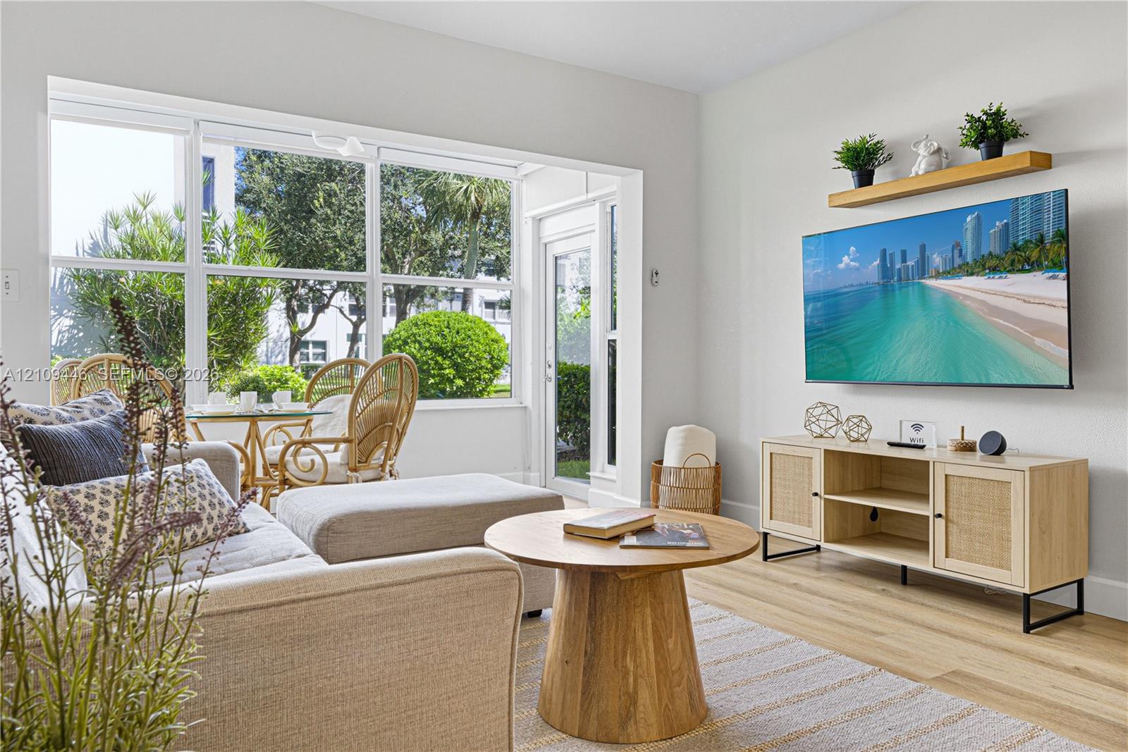 Living area featuring large windows with natural light, wood-finish flooring, and a wall-mounted floating shelf Living area featuring large windows with natural light, wood-finish flooring, and a wall-mounted floating shelf