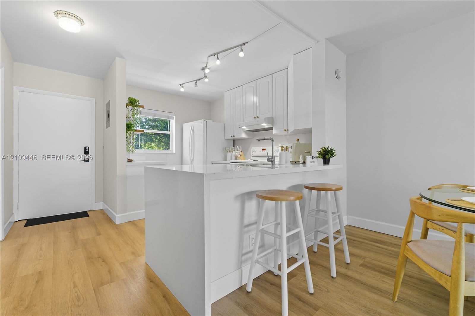 Kitchen featuring white shaker cabinetry, quartz countertops, a waterfall-edge peninsula, track lighting, and wood-finish flooring