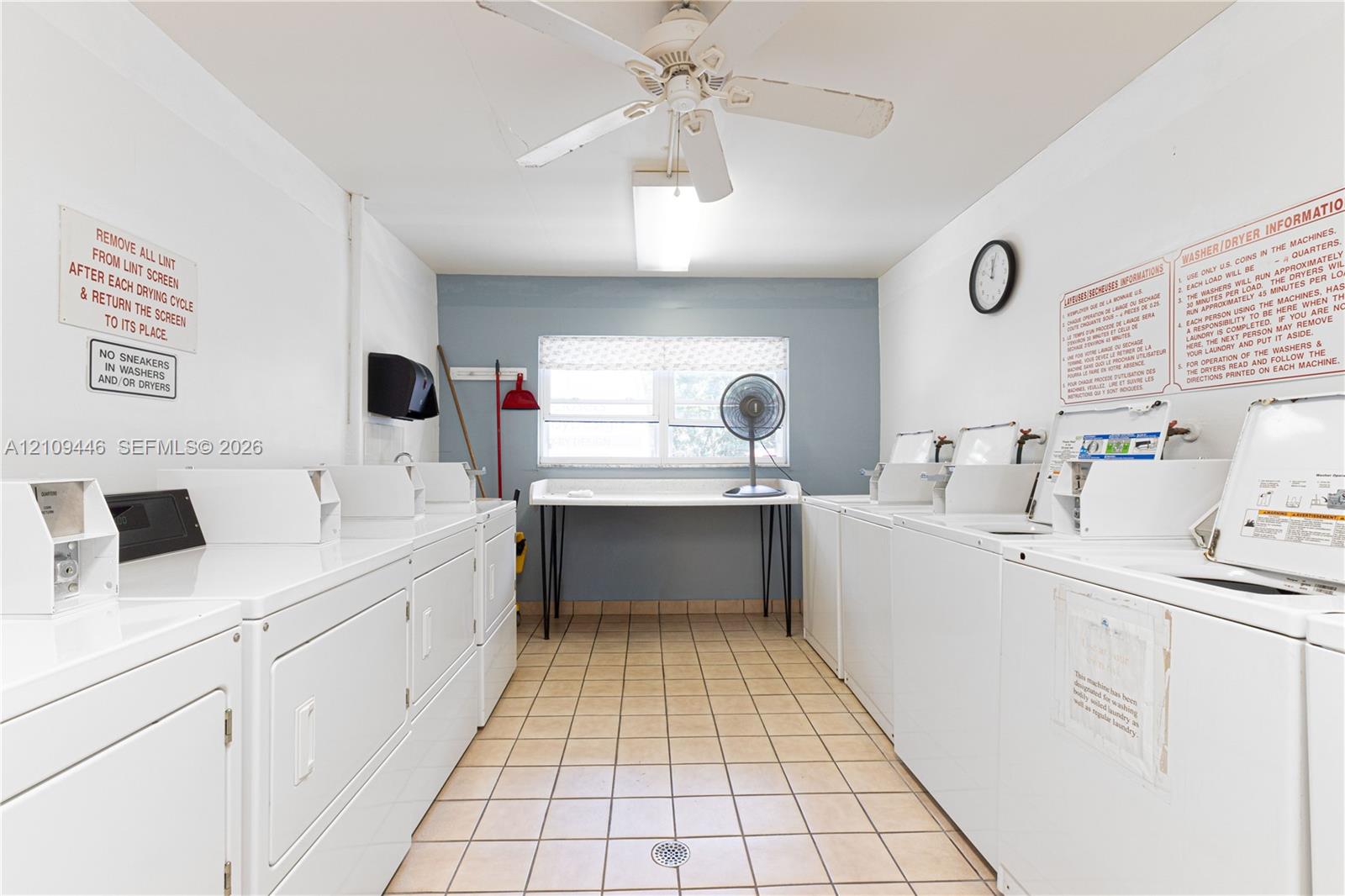 Laundry facility featuring multiple washer and dryer units, tile flooring, built-in counter space, and a ceiling fan
