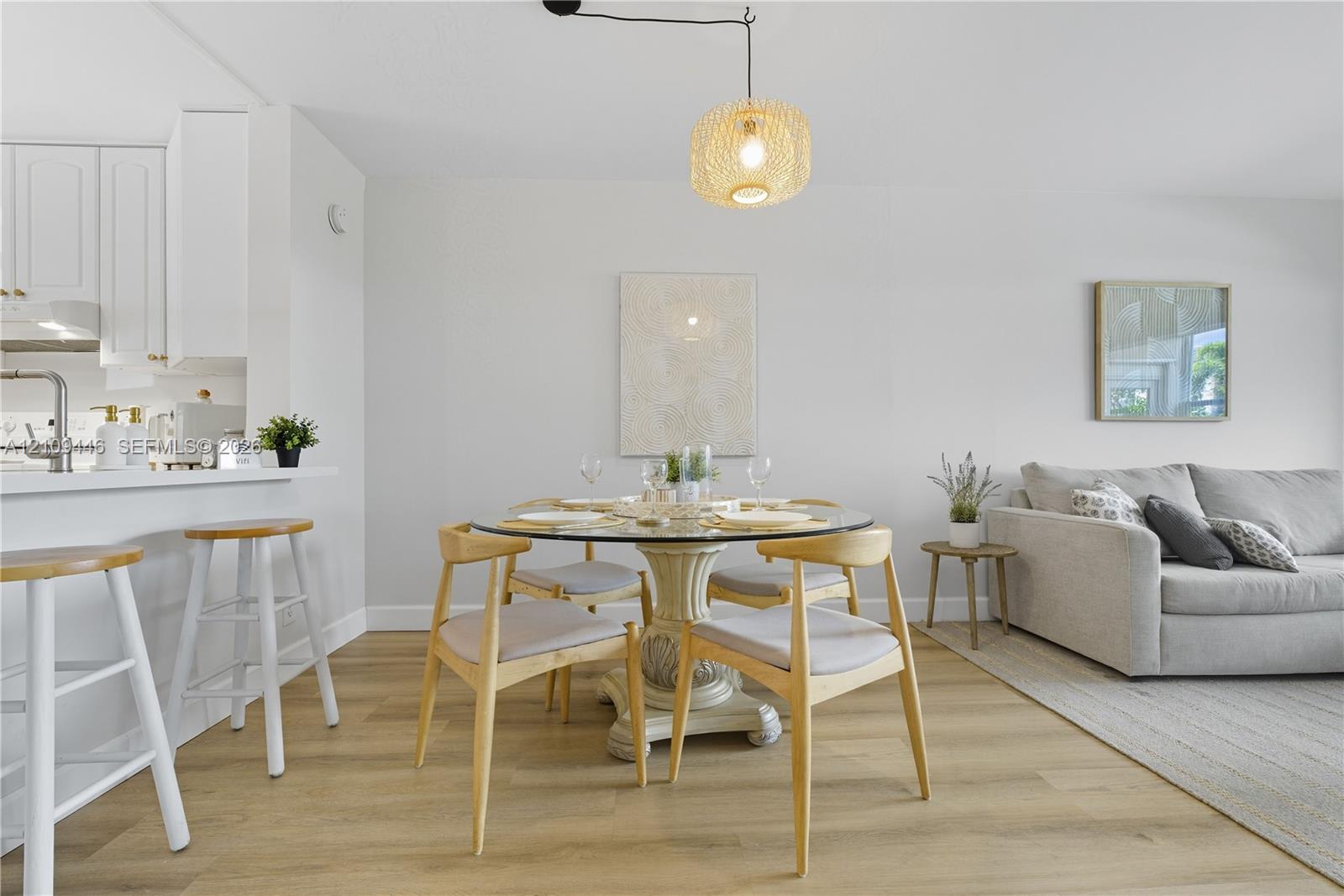 Open-concept living space featuring wood-finish flooring, a kitchen peninsula with bar-style seating, and a hanging woven pendant light fixture