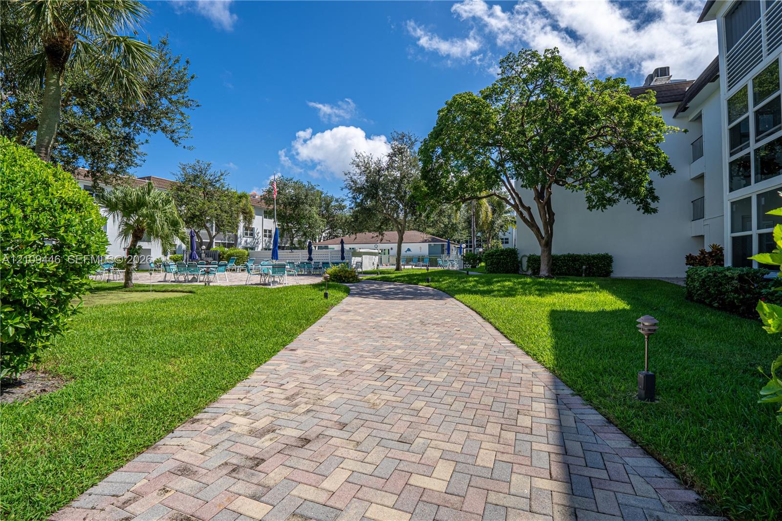 Paver walkway featuring manicured landscaping, mature trees, and exterior landscape lighting