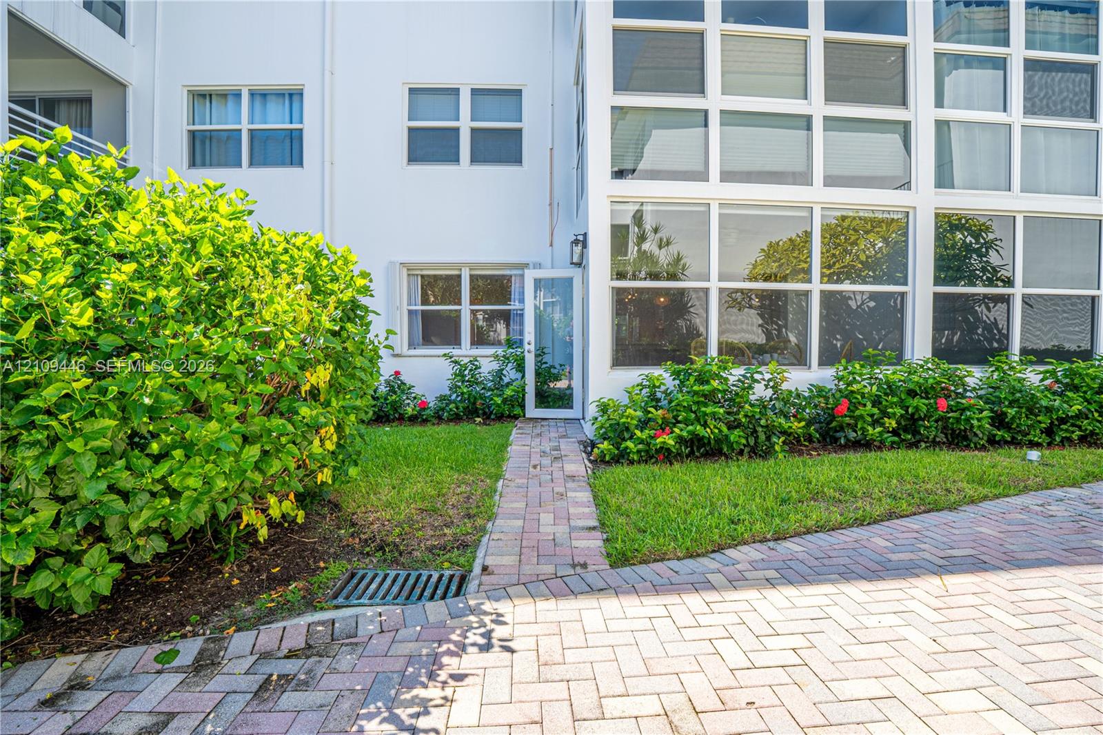 Exterior facade featuring white siding, a multi-pane glass wall, brick-style paver walkway, and manicured landscaping
