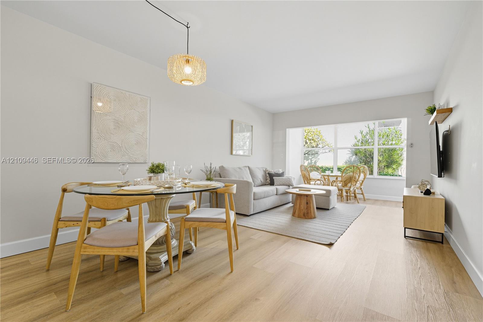 Open-concept area featuring light-toned wood-finish flooring, a large multi-pane window, and a woven pendant light fixture