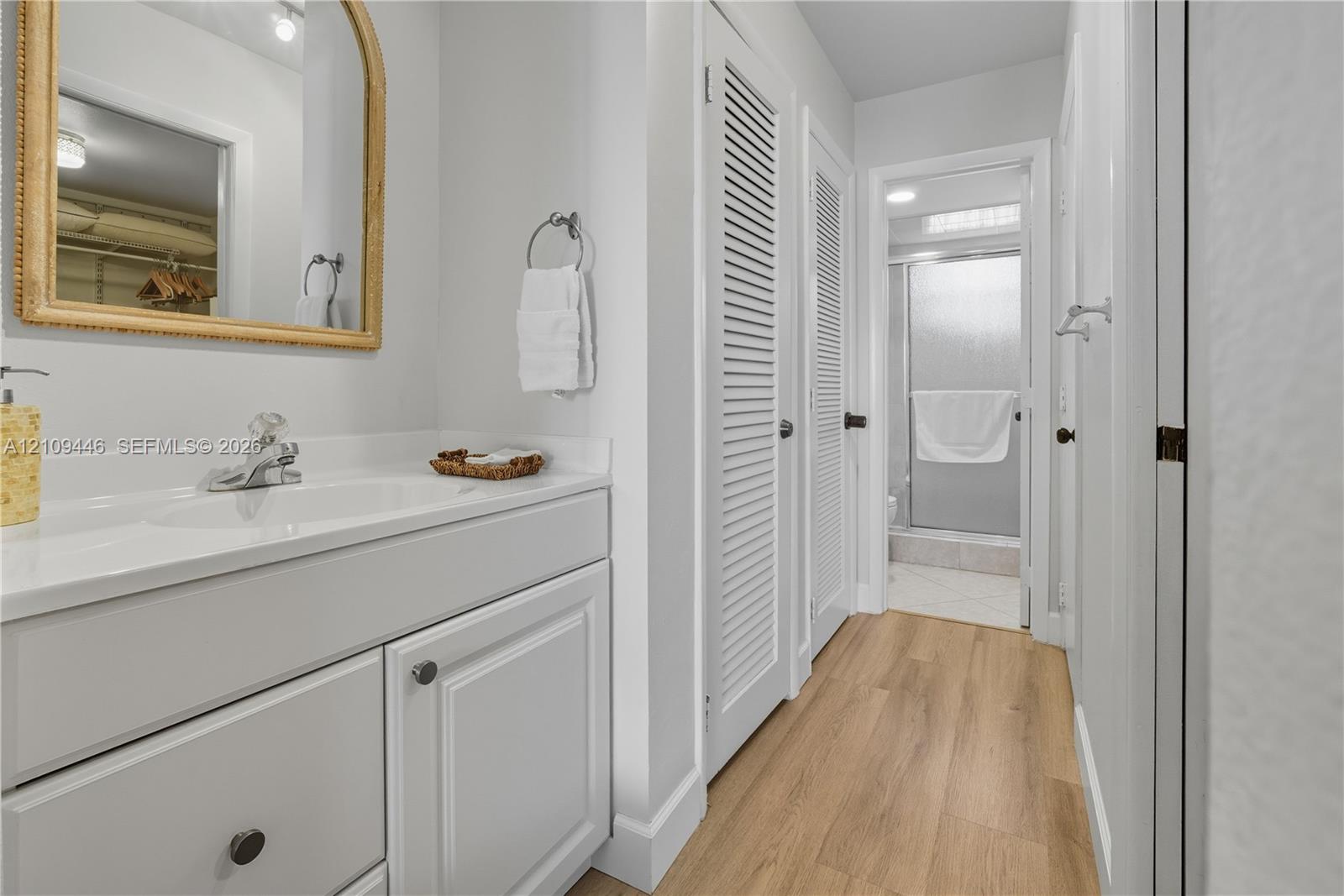 Vanity featuring a white cabinet base, countertop with an integrated sink, arched wall mirror, louvered closet doors, and wood-finish flooring