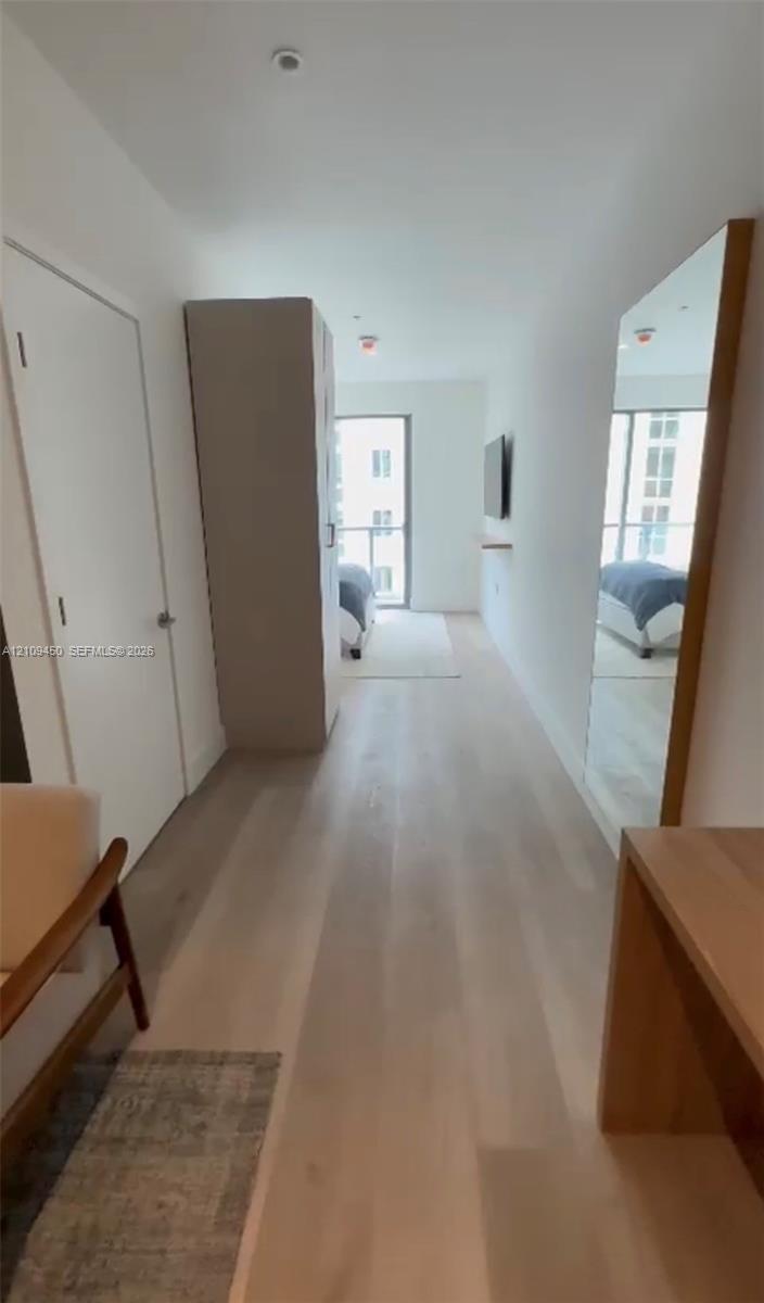 Interior space featuring light-toned wood-finish flooring, floor-to-ceiling mirror with wood frame, built-in storage cabinetry, and sliding glass door with access to an exterior balcony