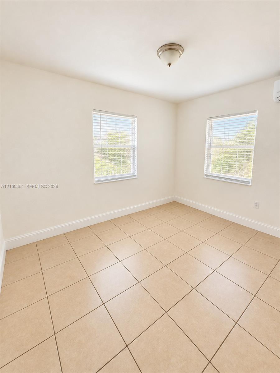 Interior space featuring large-format ceramic tile flooring, neutral wall tones, two windows with horizontal blinds, and a wall-mounted climate control unit