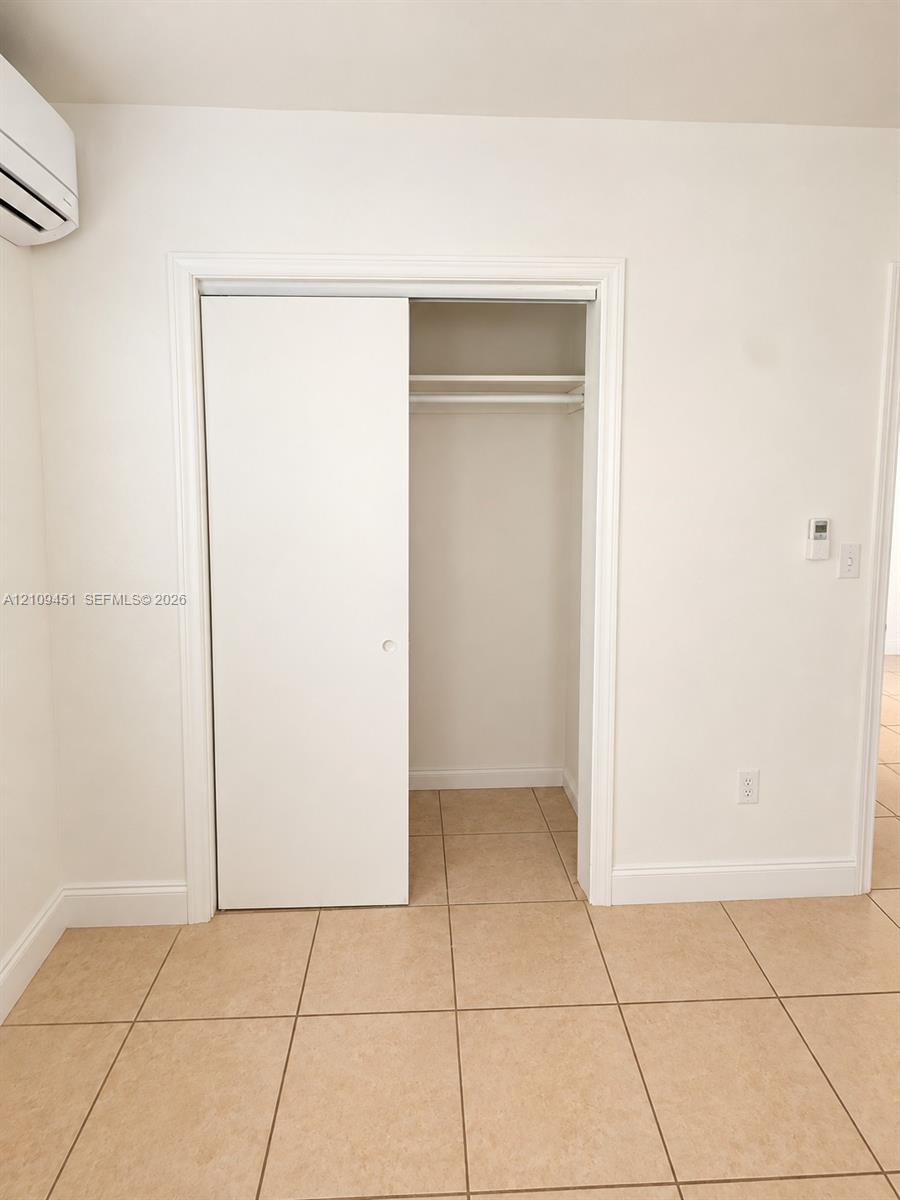 Closet featuring a sliding door and an integrated overhead shelf with hanging rod, accompanied by neutral tile flooring and a wall-mounted climate control unit