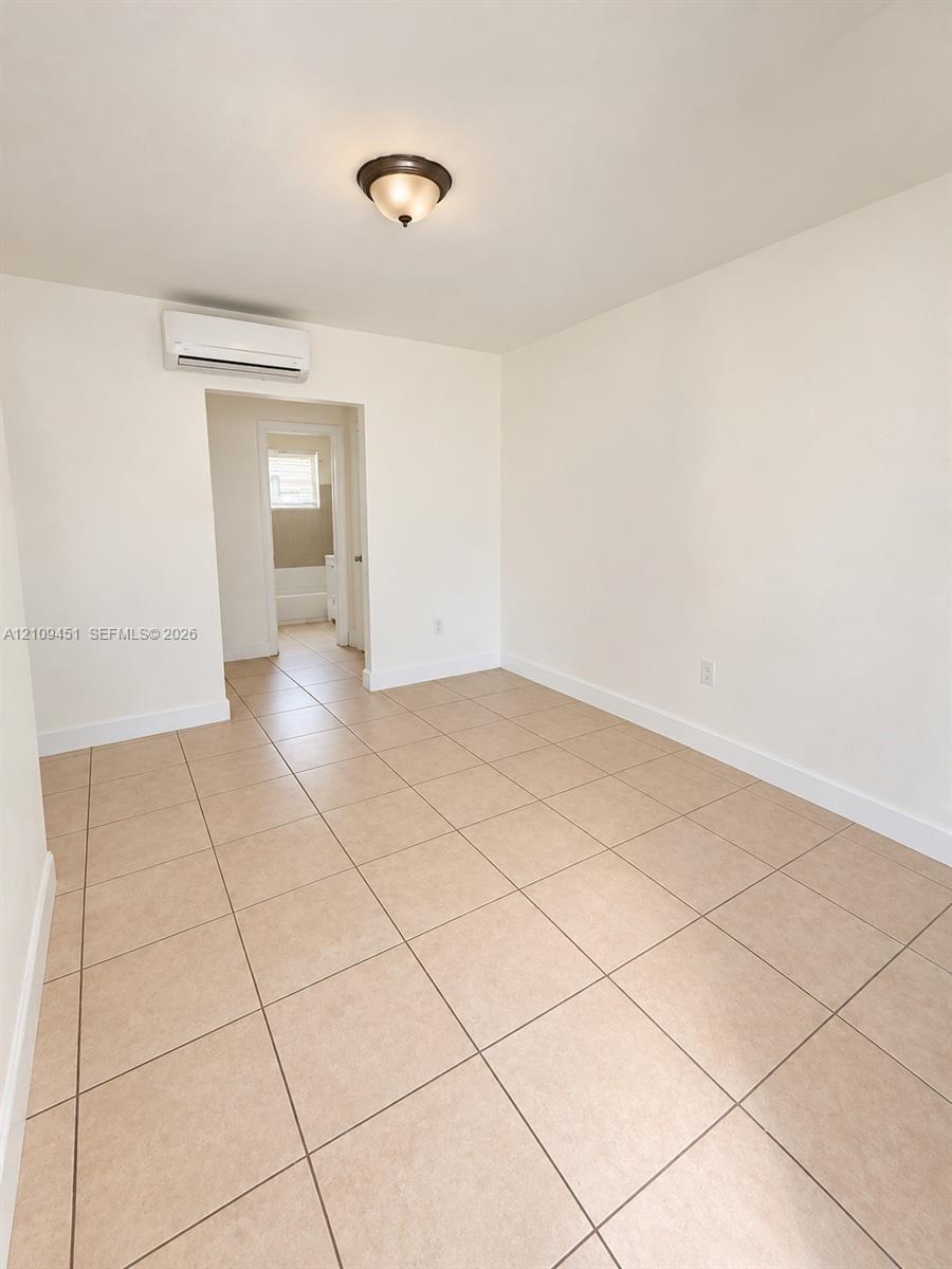 Interior space featuring neutral-toned tile flooring, white walls, wall-mounted ductless air conditioning unit, and a flush-mount light fixture