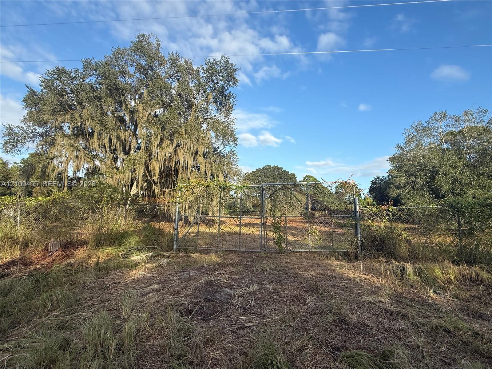 Level lot featuring chain-link perimeter fencing, gated access, and mature oak trees
