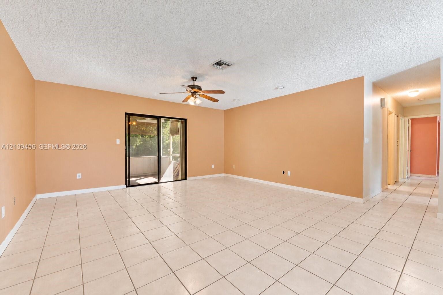 Spacious interior featuring light-toned tile flooring, recessed lighting, ceiling fan with integrated light fixture, and large sliding glass doors