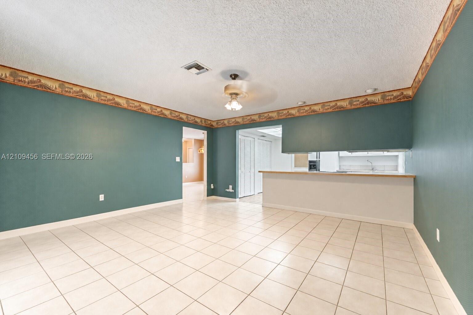 Neutral-toned ceramic tile flooring, ceiling fan with integrated lighting, and pass-through counter