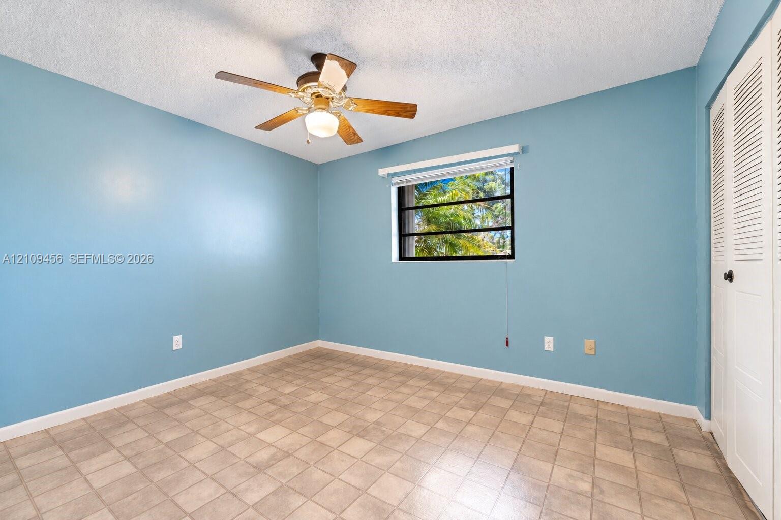 Room featuring ceramic tile flooring, a multi-blade ceiling fan with integrated lighting, and a closet with louvered bi-fold doors