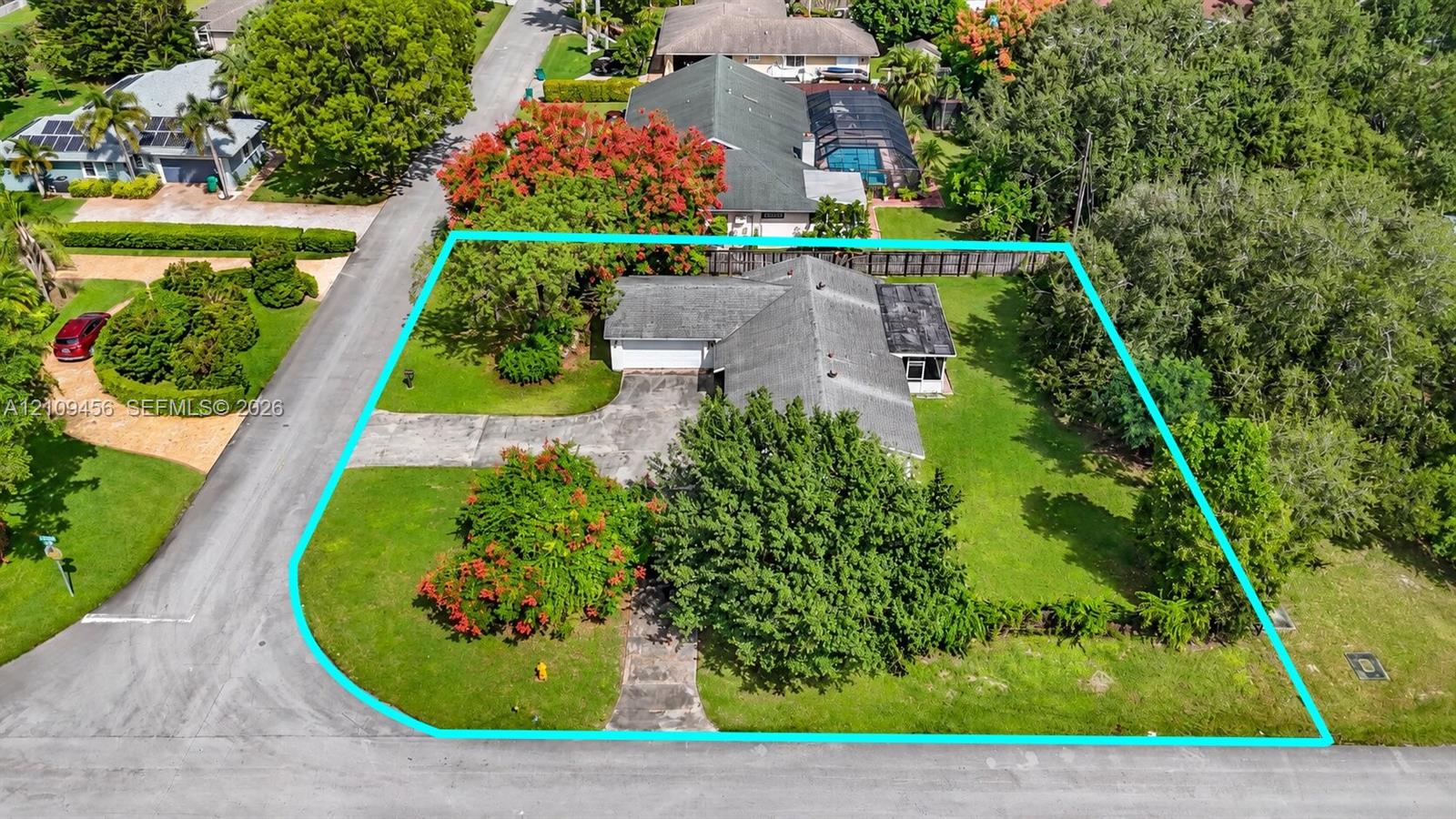 Corner lot featuring a concrete driveway, multi-gabled roofline, mature trees, and landscaping