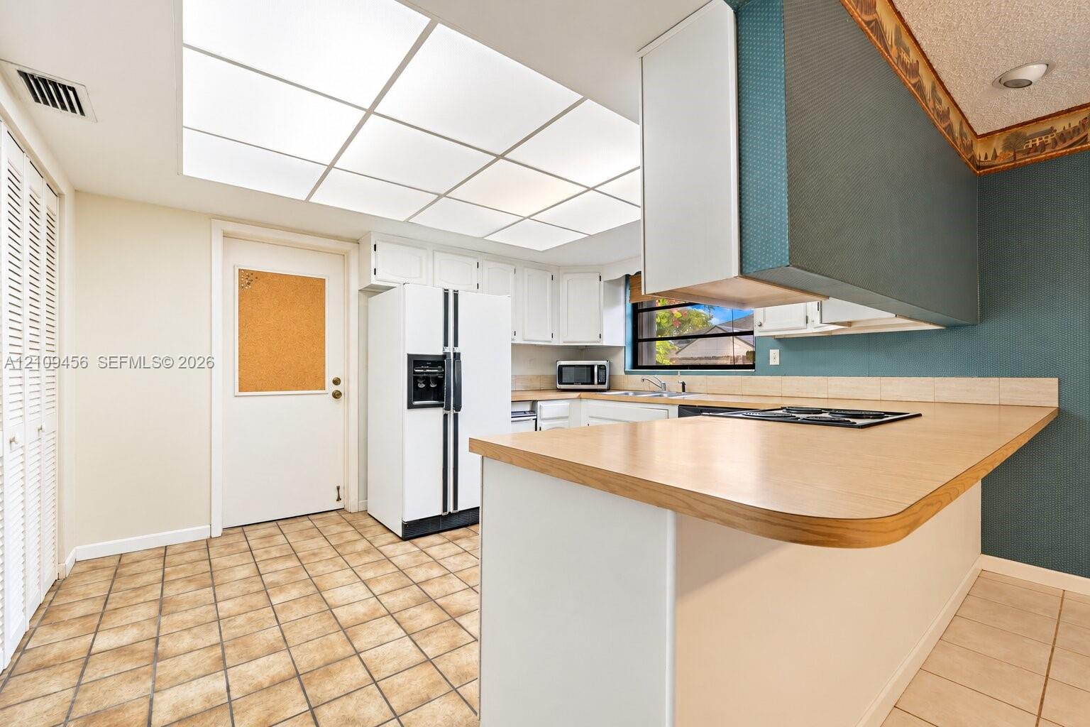 Kitchen featuring a peninsula with laminate countertop, integrated cooktop, white cabinetry, recessed grid lighting, and tile flooring