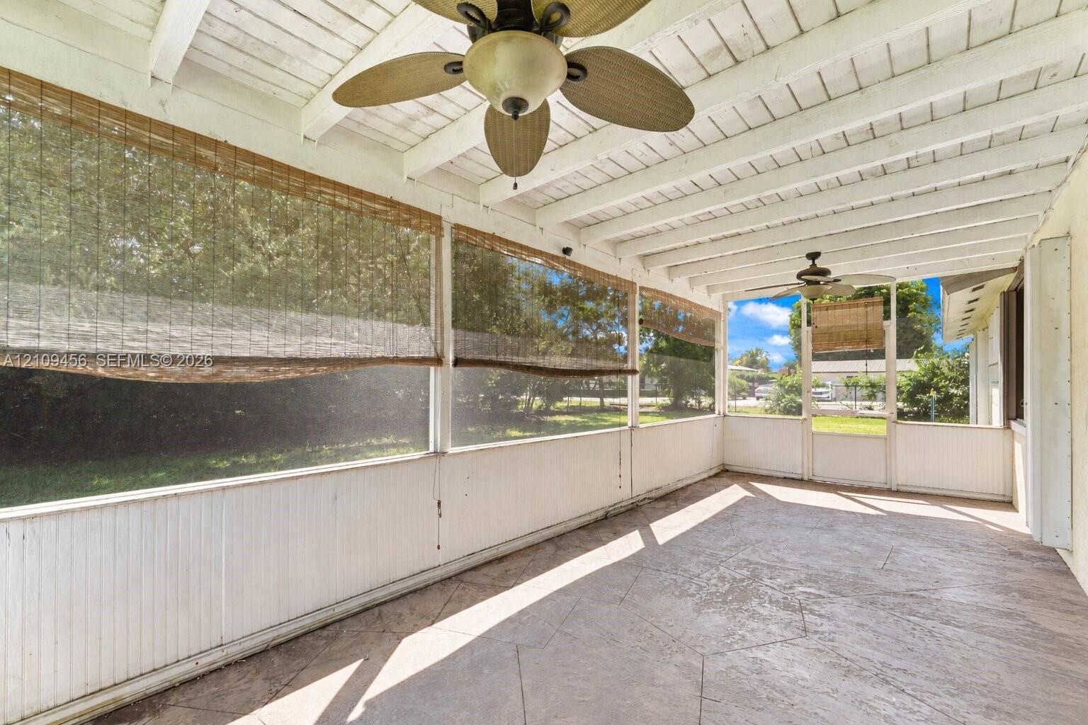 Covered porch featuring a stamped concrete floor, white beadboard wainscoting, a vaulted wood-beam ceiling, and two ceiling-mounted fans
