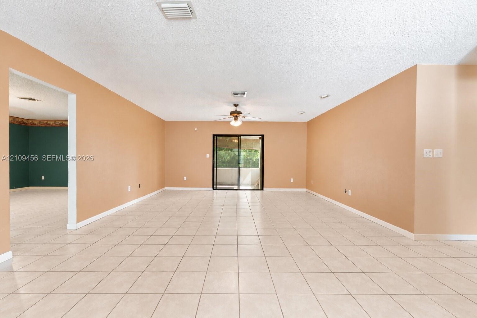 Open-concept interior featuring light-toned tile flooring, neutral wall paint, a ceiling-mounted light fixture with fan, and black-framed sliding glass doors