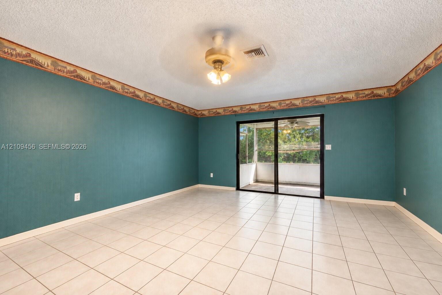 Spacious room featuring tile flooring, textured ceiling with a central multi-light ceiling fan, and sliding glass doors with access to an exterior screened enclosure
