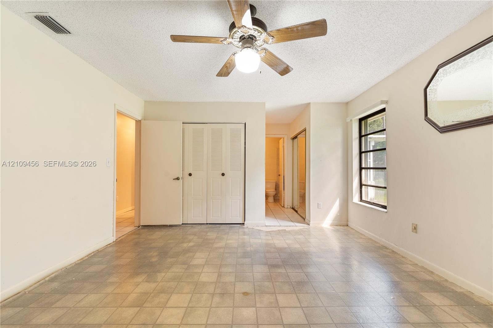 Room featuring square tile flooring, a multi-pane window, dual-panel closet doors, and a ceiling-mounted fan with integrated lighting