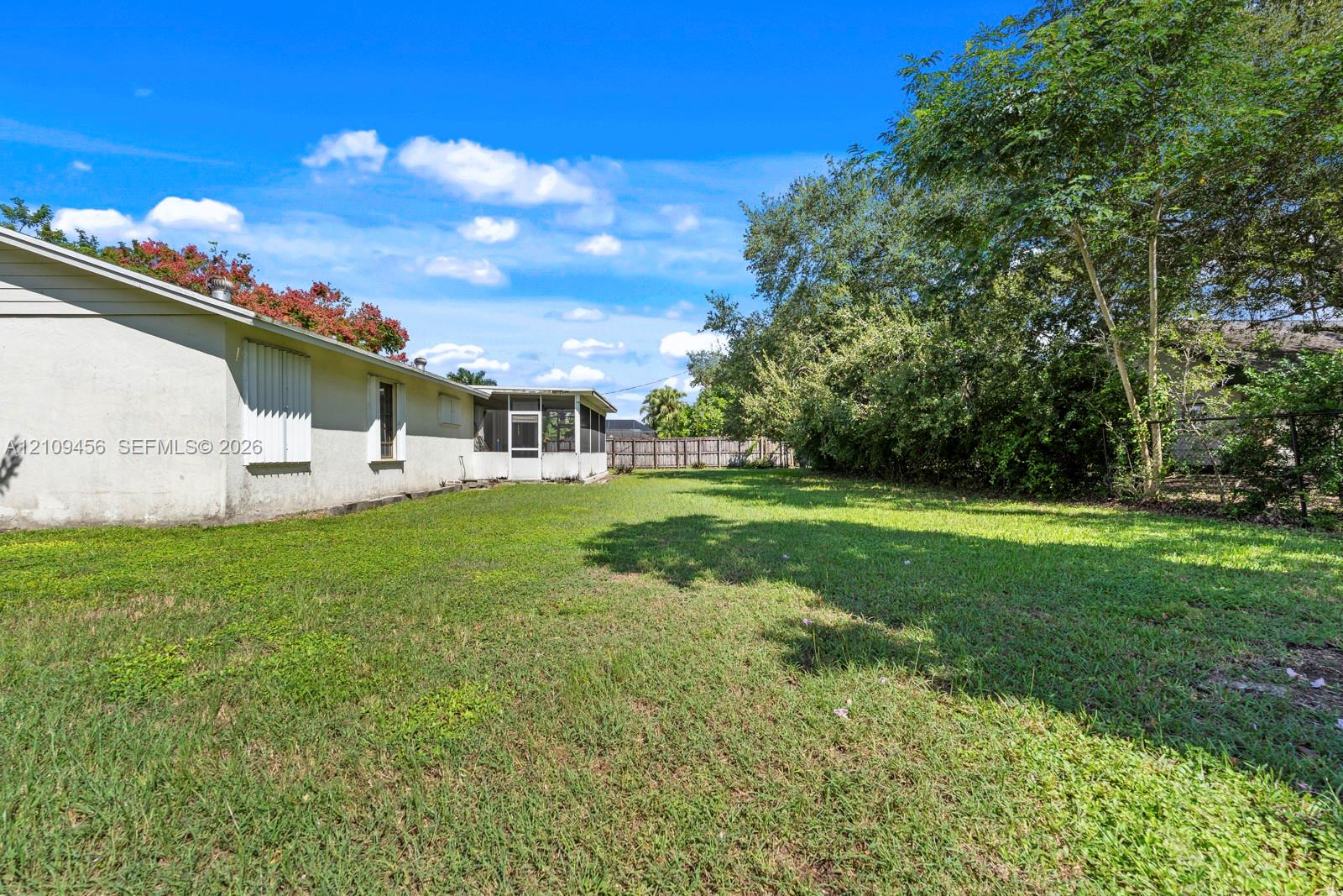 Backyard featuring a grass lawn, screen-enclosed patio, stucco exterior, mature trees, and perimeter fencing