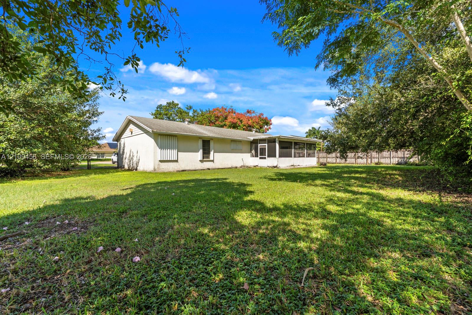 Expansive backyard featuring a sprawling lawn, mature trees, a screened-in patio, and privacy fencing