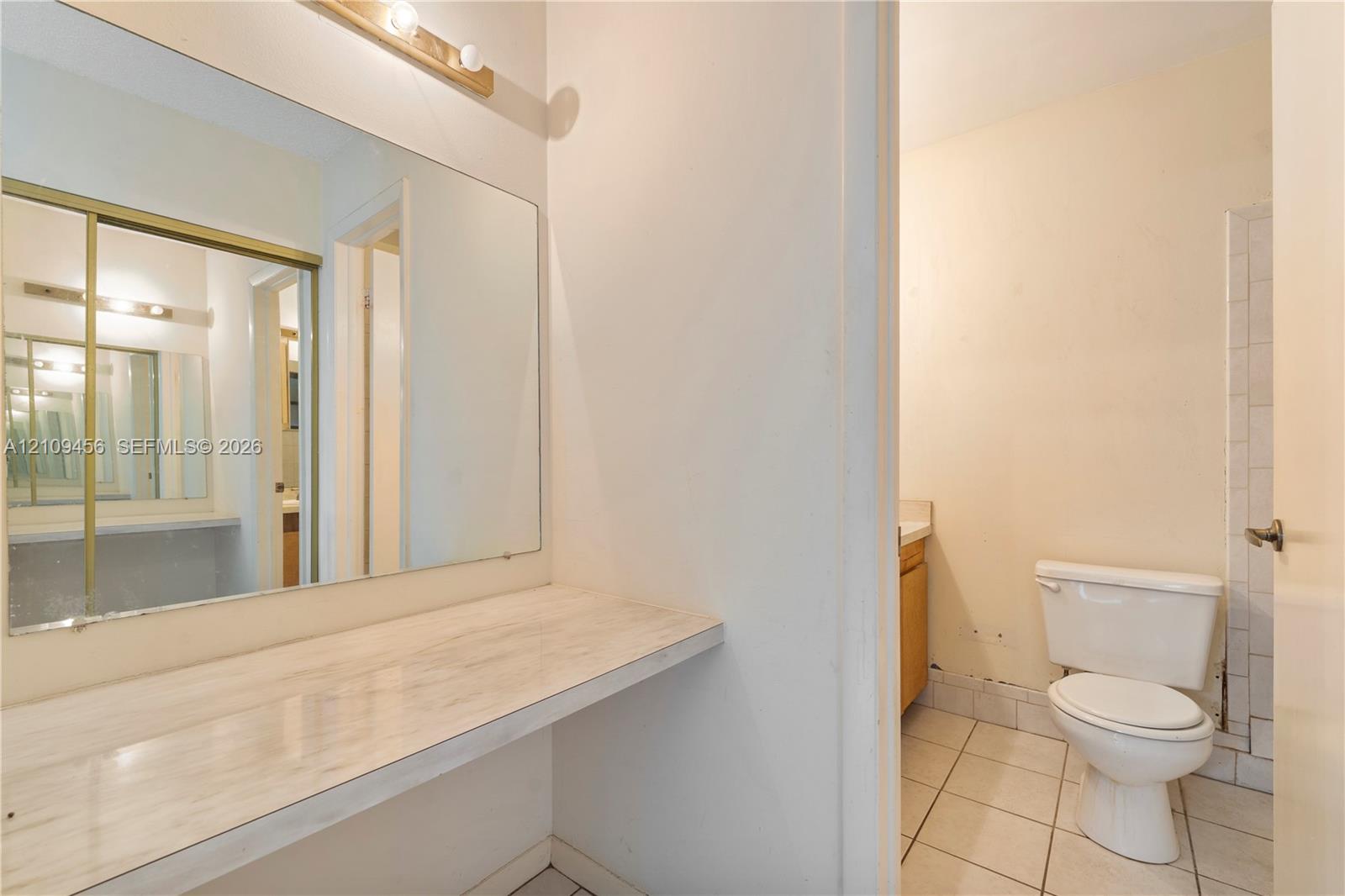 Full-width wall mirror, wood-finish countertop, tiled flooring, and porcelain toilet