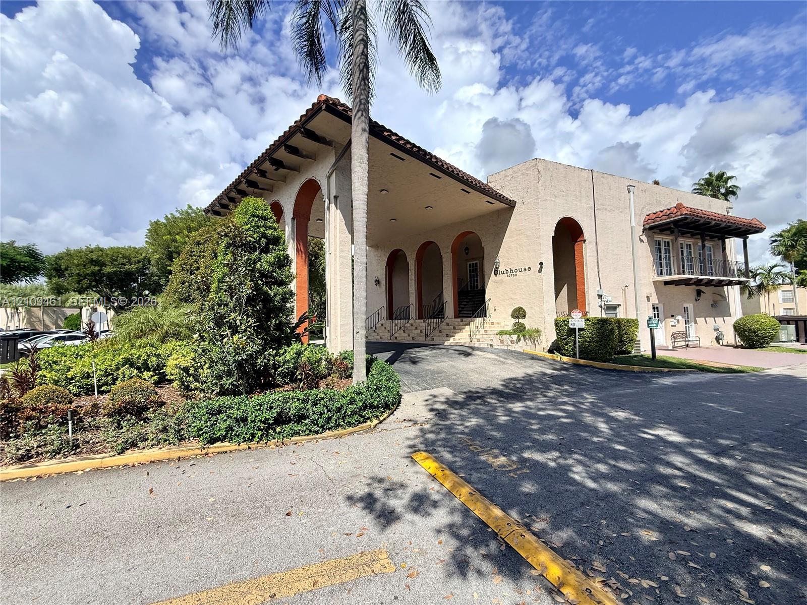 Clubhouse exterior featuring a stucco facade, decorative arched columns, tile-accented roofline, and an elevated balcony
