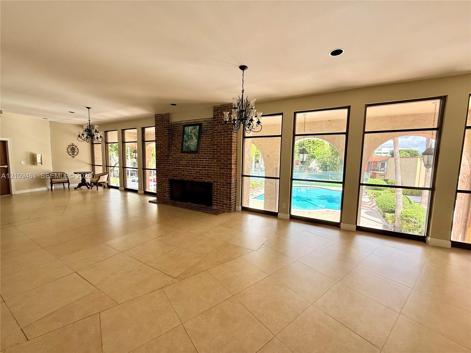 Large-format tile flooring, brick fireplace, and floor-to-ceiling windows with exterior pool access