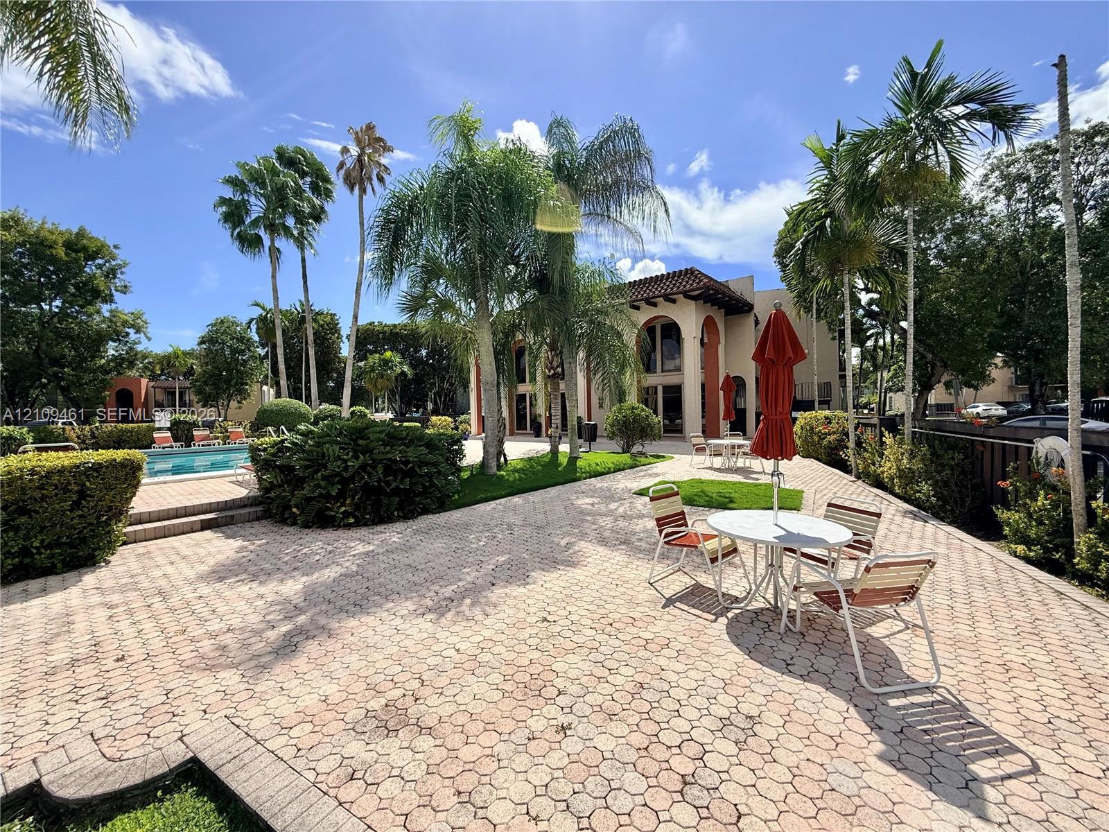 Expansive outdoor patio featuring hexagonal paver hardscaping, a swimming pool, mature palm trees, and structural arched architecture