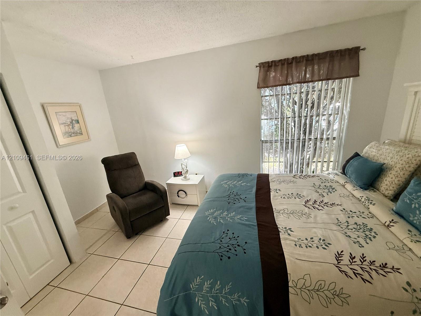 Neutral-toned ceramic tile flooring, multi-panel door with brass-finish hardware, and large sliding window with vertical blinds