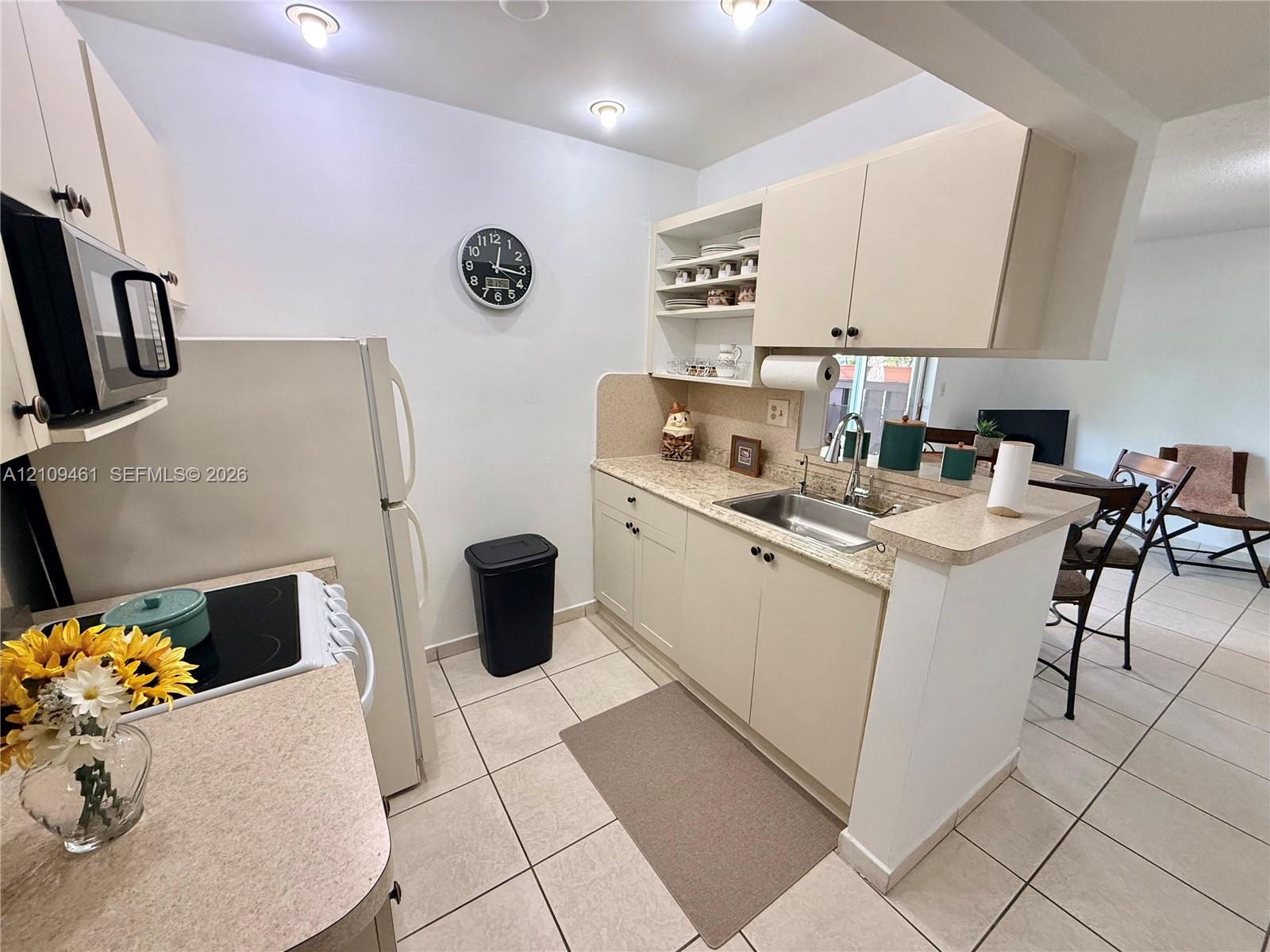 Kitchen featuring light-toned cabinetry, solid surface countertops, a stainless steel undermount sink, recessed lighting, and tile flooring